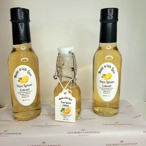 May include: Three glass bottles of pure lemon extract, two are larger and one is smaller. The bottles are clear and filled with a light yellow liquid. Each bottle has a black cap and a white label with the text "Made with Love Pure Lemon Extract" and a small lemon illustration.