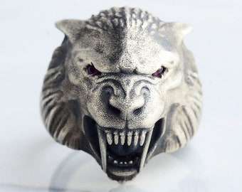 May include: A silver ring featuring a detailed wolf head design. The wolf's mouth is open, showing sharp teeth, and its eyes are red.
