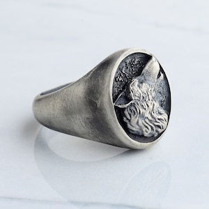 May include: A silver ring with a wolf's head design. The wolf is facing to the right and howling. The ring is made of a brushed metal.