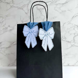 May include: Black gift bag with two blue ribbon gift tags. The tags have the name "Alexandra" written on them. One tag also has the words "Something Blue" written on it.