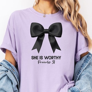 May include: A lavender t-shirt with a black bow and the text "She is worthy Proverbs 31" printed on the front.