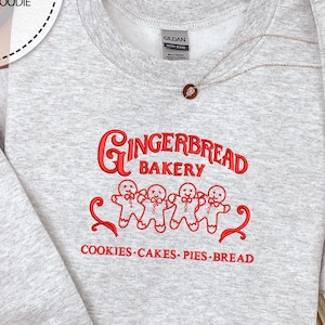 May include: A gray sweatshirt with red embroidered text that reads "Gingerbread Bakery" with four gingerbread men and the words "Cookies-Cakes-Pies-Bread".