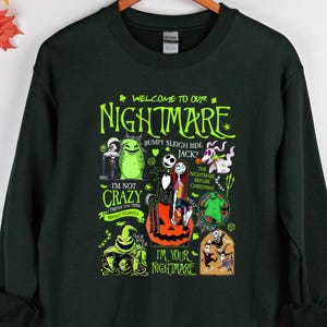 May include: Dark green sweatshirt with a graphic featuring characters and text from "The Nightmare Before Christmas." The design includes the words "Welcome to our Nightmare" and "I'm not crazy, I'm your nightmare."