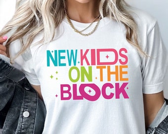 May include: White t-shirt with the text "NEW KIDS ON THE BLOCK" in colorful letters with a YouTube play button icon in the "O" of "BLOCK".