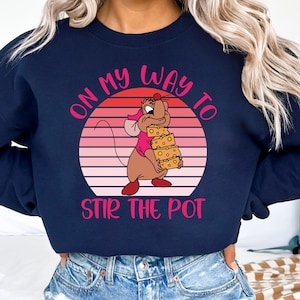 May include: A navy blue sweatshirt with a pink and white graphic of a cartoon mouse holding a stack of cheese. The graphic is in a circle with the text "On my way to stir the pot" in pink.