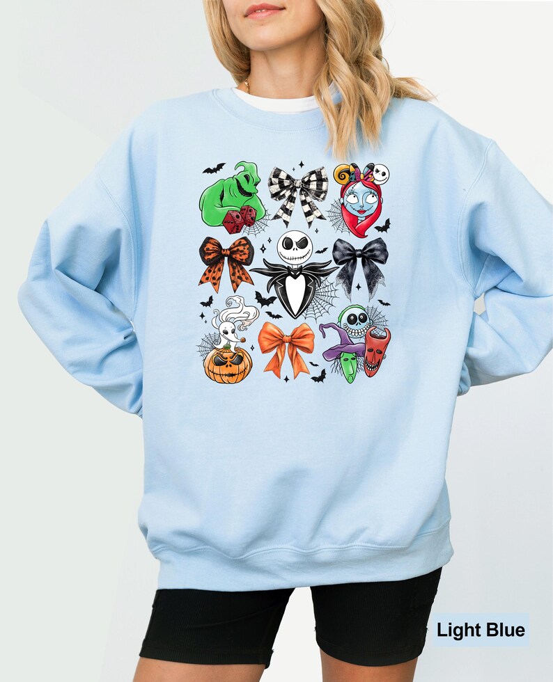 May include: Pale blue sweatshirt with a pattern of cartoon character bows, including Jack Skellington and Sally. The design is surrounded by bats and spiderwebs. The text "Light Blue" is at the bottom of the image.