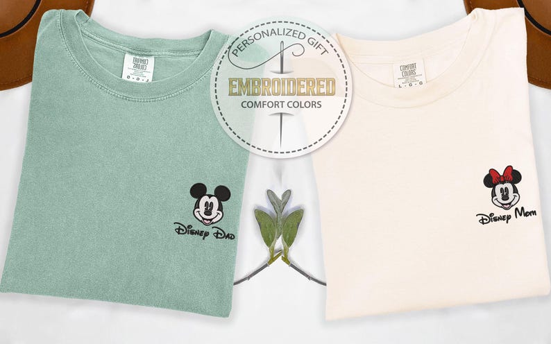 May include: Two embroidered Comfort Colors t-shirts, one mint green with a Mickey Mouse design and the text "Disney Dad", and one cream-colored with a Minnie Mouse design and the text "Disney Mom". A circular emblem reads "Personalized Gift, Embroidered, Comfort Colors".