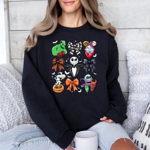 May include: Black sweatshirt with a colourful collage of Halloween-themed character bows. The design includes images of Jack Skellington, Sally, Oogie Boogie, and other characters from The Nightmare Before Christmas. The bows are in various colours and styles.