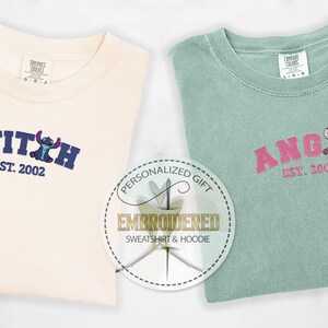Puede incluir: Dos camisetas bordadas con un dise&ntilde;o de personaje de Stitch. La primera camiseta es crema con bordado azul y el texto "STITCH EST. 2002". La segunda camiseta es verde claro con bordado rosa y el texto "ANGEL EST. 2002".
