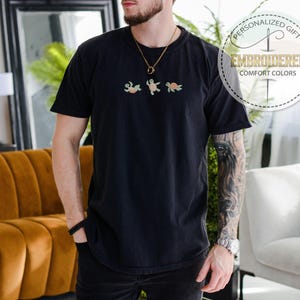 May include: Black t-shirt with embroidered turtles in shades of green and tan. The shirt has a crew neck and short sleeves. The text "Personalized Gift" and "Embroidered Comfort Colors" is printed on the upper right side.