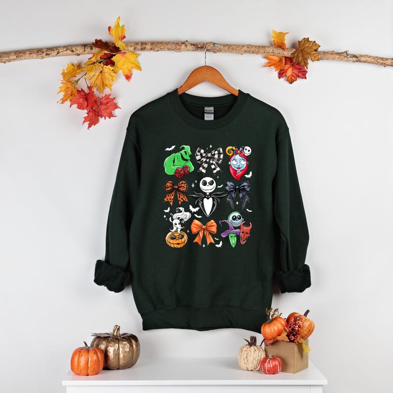 May include: Dark green sweatshirt with a colourful graphic of characters and bows from The Nightmare Before Christmas. The design includes Jack Skellington, Sally, and other iconic elements. A festive apparel item for fans of the movie.