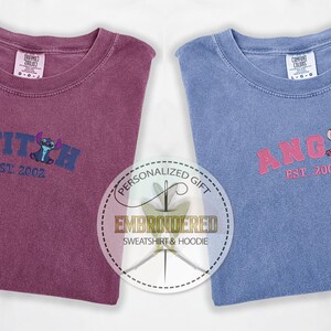 Puede incluir: Dos camisetas bordadas, una granate y otra azul, con el texto "STITCH EST. 2002" y "ANGEL EST. 2002" en una fuente de estilo universitario. Cada camiseta presenta un personaje de dibujos animados de la pel&iacute;cula de Disney Lilo & Stitch.