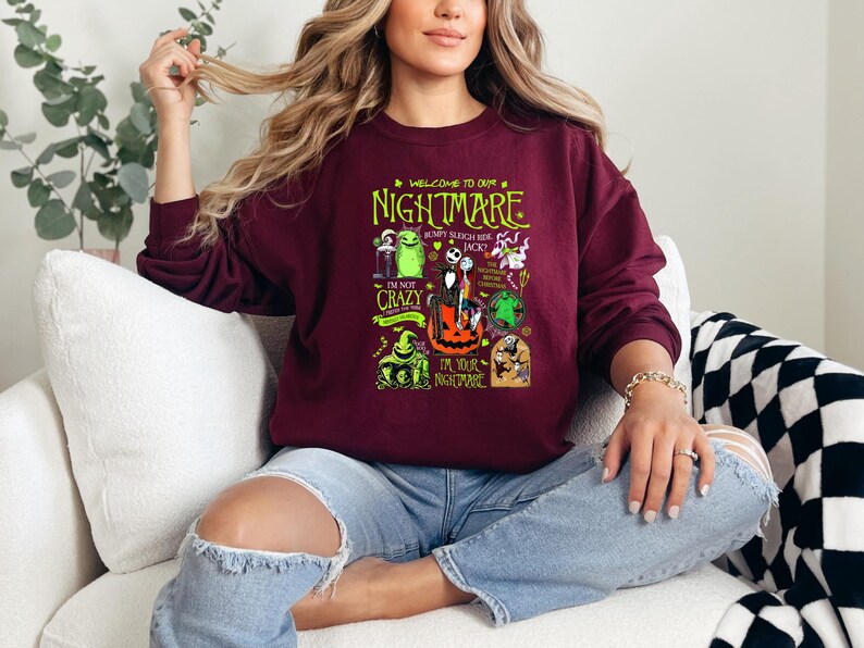 May include: Burgundy crew neck sweatshirt featuring a graphic from "The Nightmare Before Christmas." The design includes characters like Jack Skellington, Sally, and Oogie Boogie, with text that reads "Welcome to our Nightmare."