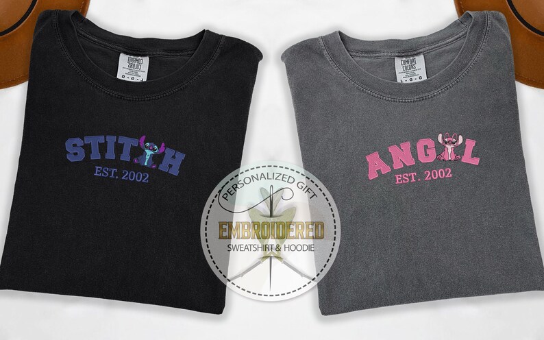 Puede incluir: Dos camisetas grises con dise&ntilde;os bordados. La camiseta de la izquierda tiene un dise&ntilde;o de Stitch azul y morado con el texto "STITCH EST. 2002". La camiseta de la derecha tiene un dise&ntilde;o de Angel rosa con el texto "ANGEL EST. 2002".