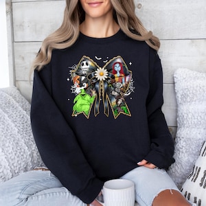 May include: Black crew neck sweatshirt featuring a large bow design with characters from The Nightmare Before Christmas. The bow is black with gold trim and a white daisy in the center. The characters include Jack Skellington, Sally, and Oogie Boogie.