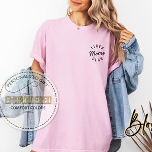 May include: A pink t-shirt with the text "Tired Moms Club" in a circle on the front.