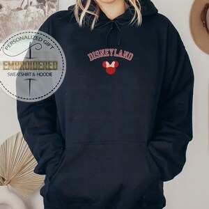 May include: Black hooded sweatshirt with the text "DISNEYLAND" in red and white lettering and a red Mickey Mouse head with a white bow on the front.