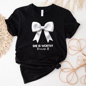 May include: Black t-shirt with a white bow and the text "She is worthy Proverbs 31" printed on the front.