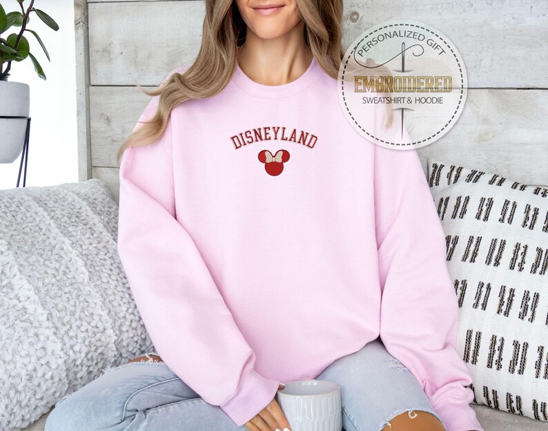 May include: Pink sweatshirt with the text "DISNEYLAND" in red and a red embroidered Mickey Mouse head with a bow.