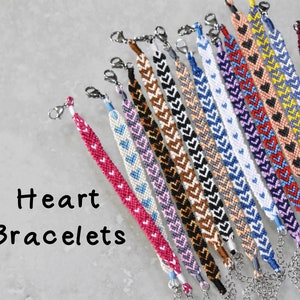 Könnte beinhalten: Eine Sammlung bunter Freundschaftsarmbänder mit Herzmustern. Die Armbänder sind aus buntem Stickgarn gefertigt und haben silberne Verschlüsse.