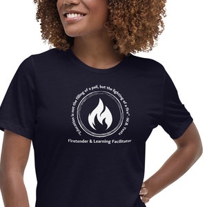 May include: A navy blue t-shirt with a white circle graphic featuring a flame and the text "Inspiration is not the filling of a pail, but the lighting of a fire within."  "Fire-tender & Learning Facilitator"