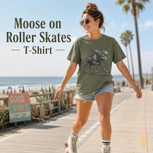 May include: An olive green short-sleeve t-shirt featuring a black and white graphic illustration of a moose wearing roller skates. The shirt has a crew neckline and a relaxed fit, showcasing a detailed sketch of the animal in motion on the front.