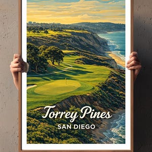 May include: A framed print of Torrey Pines in San Diego. The artwork depicts a golf course overlooking the ocean, with vibrant green fairways and a blue sea. The sky transitions from yellow to blue.