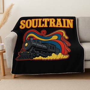 May include: Black throw blanket featuring a retro illustration of a black steam train with the text "SOULTRAIN" in yellow and orange. The design includes red, blue, and yellow swirls, and yellow smoke.