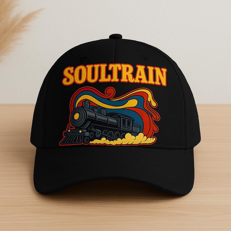 May include: Black baseball cap featuring a retro design with the word "SOULTRAIN" in yellow and a stylized illustration of a black steam train with colorful smoke trails. The cap has a curved brim.