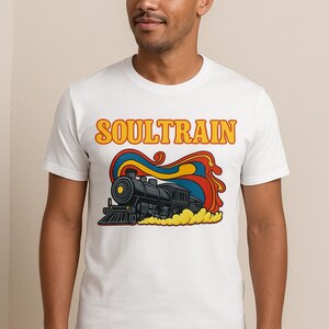 May include: White t-shirt featuring a retro illustration of a black steam train with the word "SOULTRAIN" in orange and yellow. The design includes red, blue, and yellow smoke-like elements, creating a vintage aesthetic.