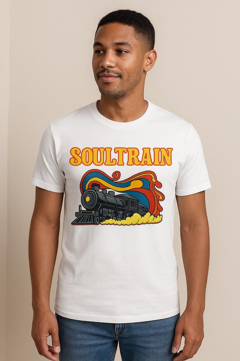 May include: White t-shirt featuring a retro illustration of a black steam train with the word "SOULTRAIN" in orange and yellow. The design includes red, blue, and yellow smoke-like elements, creating a vintage aesthetic.