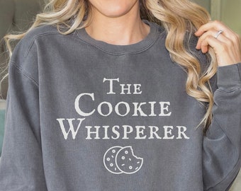 May include: A gray sweatshirt with the text "The Cookie Whisperer" and a white outline of two cookies.