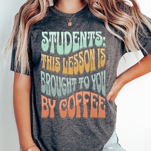May include: A grey t-shirt with the text "Students: This lesson is brought to you by coffee" in a colourful retro font.