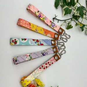 May include: Five colourful fabric keychains with metal key rings. Each keychain features a different floral pattern and is made of patchwork fabric.