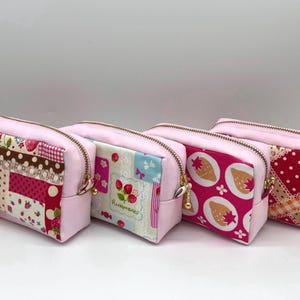 May include: Four pink zipped pouches with different fabric patterns. The patterns include strawberries, polka dots, and patchwork designs. Each pouch has a gold-coloured zip and a pink base. The pouches are arranged in a row.