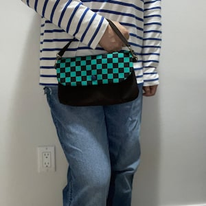 May include: A black and green checkered crossbody bag with a black strap. The bag has a flap with a button closure.