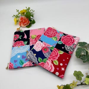 May include: Two patchwork fabric pouches with floral patterns. One pouch features a black, pink, and blue design with a lace accent and a gold zip. The other pouch has a red, blue, and pink floral pattern.