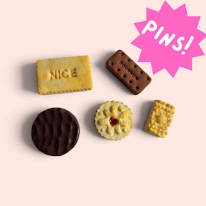 May include: Five biscuit-shaped pins featuring a rectangular yellow NICE biscuit, a rectangular brown BOURBON biscuit, a round dark brown biscuit, a round light-coloured biscuit with a red centre, and a small rectangular textured biscuit.