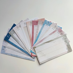 Könnte beinhalten: Ein Fächer mit Budgetblättern mit Aquarellhintergründen in verschiedenen Blautönen, Rosa- und Grautönen. Jedes Blatt hat einen Bereich für "Datum" und "Summe". Der Text "Budget Sheet" ist oben rechts auf dem Blatt gedruckt.