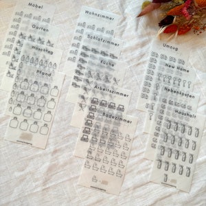 Könnte beinhalten: Ein Set mit 10 transparenten Aufklebern mit schwarzen Umrissen verschiedener Symbole. Die Symbole umfassen Möbel, Haushaltsgegenstände und andere gängige Ausgaben. Die Blätter sind mit deutschen Wörtern wie "Möbel", "Wohnzimmer", "Schlafzimmer", "Küche", "Arbeitszimmer", "Badezimmer", "Garten", "Waschtag", "Pfand", "Umzug", "New Home", "Nebenkosten" und "Haushalt" beschriftet.