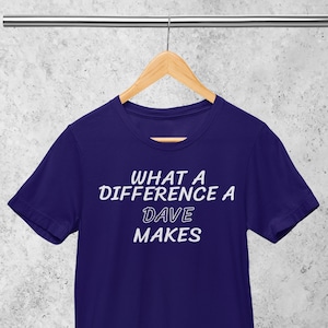 Könnte beinhalten: Ein lila T-Shirt mit dem Text "WHAT A DIFFERENCE A DAVE MAKES" in Weiß.