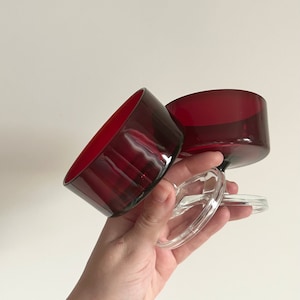 May include: Two red glass dessert bowls with clear glass stems. The bowls are stacked on top of each other.