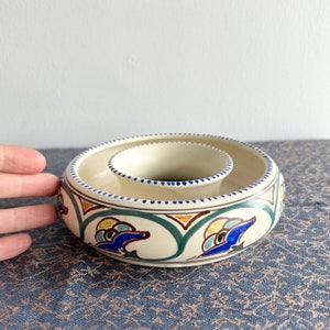 May include: A white ceramic bowl with a blue, green, and yellow geometric design. The bowl has a smaller bowl inside, creating a double-tiered design.