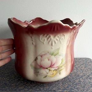 May include: A vintage ceramic planter with a scalloped rim and a floral design. The planter is painted in shades of red, white, and green.
