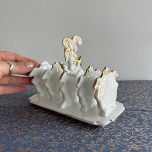 Peut inclure: Porte-couteaux à pain en porcelaine blanche avec une bordure dorée et un dessus décoratif. Le porte-couteaux a quatre fentes pour les couteaux.