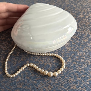 May include: A white ceramic clam shell box with a pearl necklace draped over it.