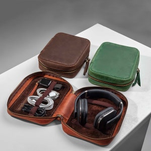 May include: Three leather zippered pouches in brown, green, and orange. The orange pouch is open and contains a pair of headphones and various cords.