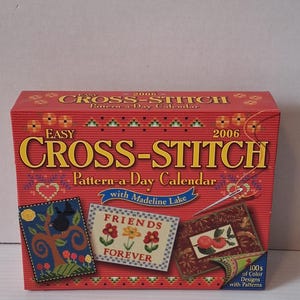 May include: A red box for a 2006 Easy Cross-Stitch Pattern-a-Day Calendar. The box features the text "CROSS-STITCH" in yellow and the text "Pattern-a-Day Calendar" in white. The box also features three small cross-stitch designs.