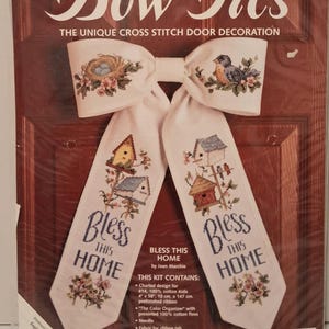 May include: A cross-stitch door decoration kit titled "Bow Ties." The white bow features embroidered birds and a nest. The tails read "Bless This Home" with birdhouse designs. Finished size is 11" x 17".