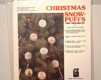 May include: A Christmas Snow Puffs tree ornament kit by Saddle Valley Stitchery. The kit includes pre-embroidered ornaments, white broadcloth backing, embroidery floss, and instructions. The package shows finished ornaments on a Christmas tree.